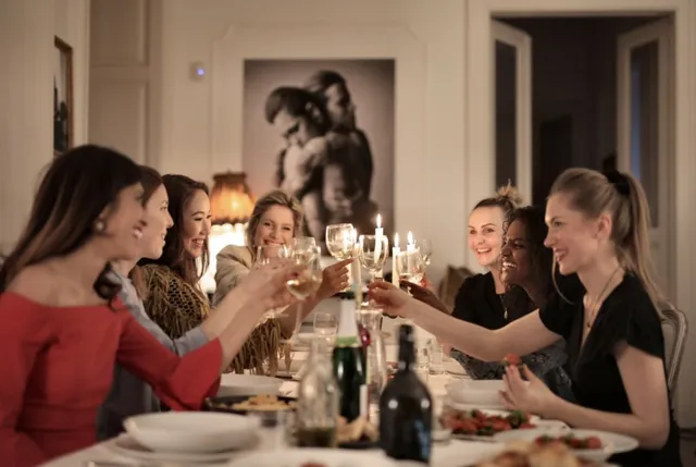 Un grup de femei stă la o masă din interior și ridică pahare de sticlă pentru un toast.