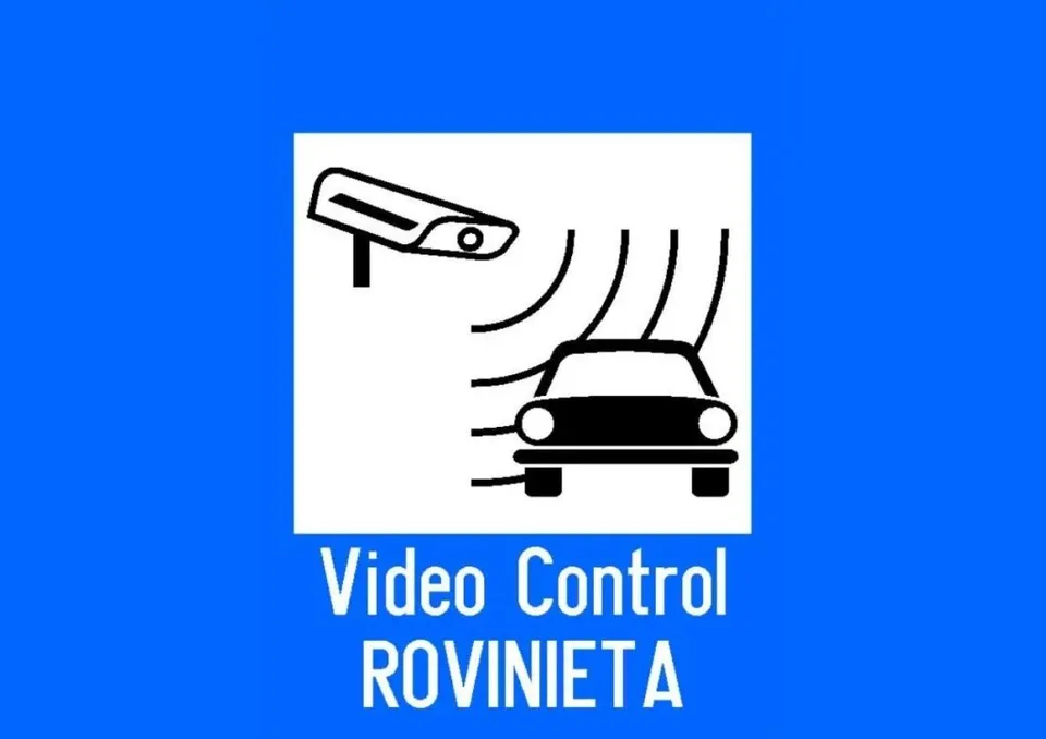 Un semn alb cu pictograme negre reprezentând o cameră de supraveghere și un autoturism, situat pe un fundal albastru cu text alb.