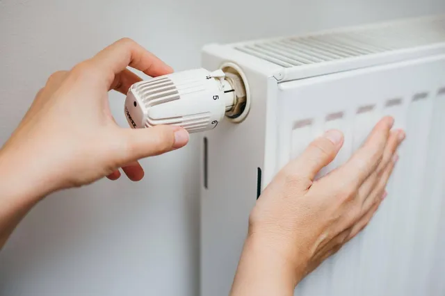 Două mâini ating un radiator alb, una rotind robinetul termostatic și cealaltă apăsând pe partea laterală a obiectului.