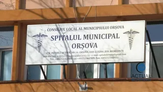 Un panou alb afișează textul Spitalul Municipal Orșova și simboluri caduceu pe o clădire cu ferestre și structură portocalie.