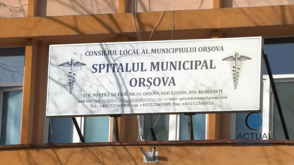 Un panou alb afișează textul Spitalul Municipal Orșova și simboluri caduceu pe o clădire cu ferestre și structură portocalie.