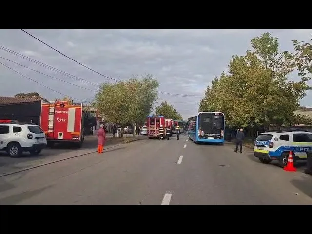 Un autobuz albastru și un vehicul de poliție sunt parcate pe un drum lângă un camion de pompieri și un vehicul de intervenție roșu.