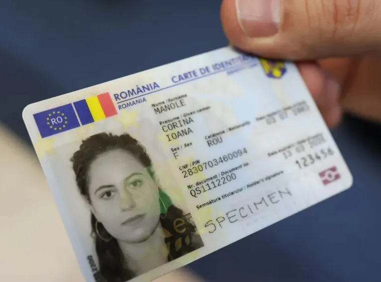 O mână ține cartea electronică de identitate a României, care afișează o poză a unei femei, date personale și cuvântul SPECIMEN.