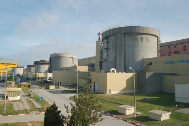 Mai multe structuri cilindrice de beton gri sunt situate lângă clădiri industriale de culoare galbenă sub un cer înzăpezit.