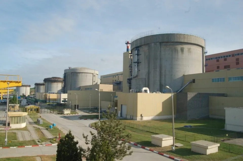 Mai multe structuri cilindrice de beton gri sunt situate lângă clădiri industriale de culoare galbenă sub un cer înzăpezit.