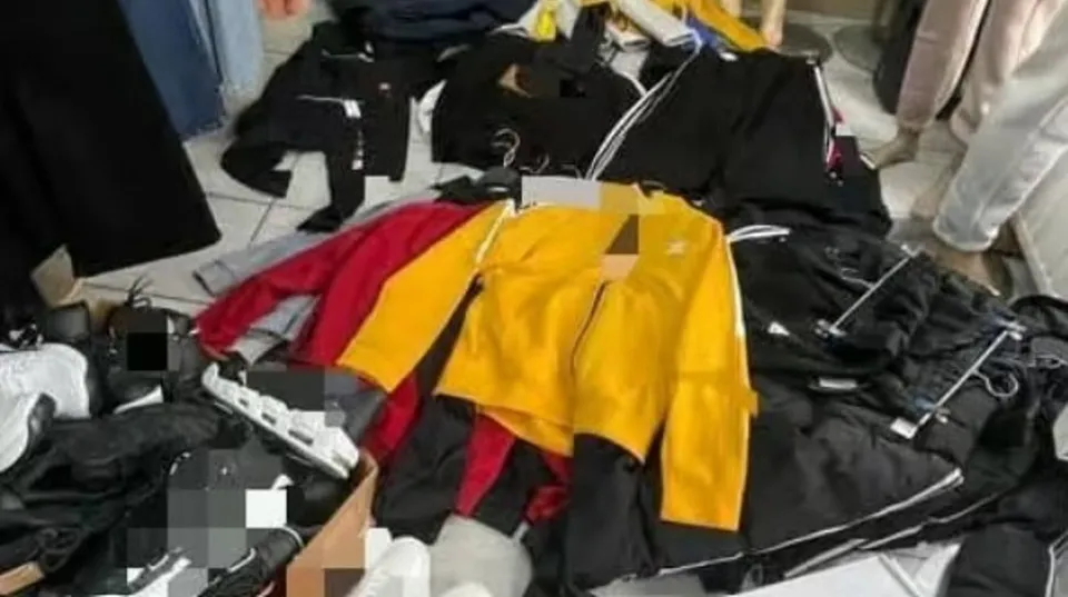 Diverse haine de culori negre, roșii și galbene sunt întinse pe un podea într-un spațiu interior.