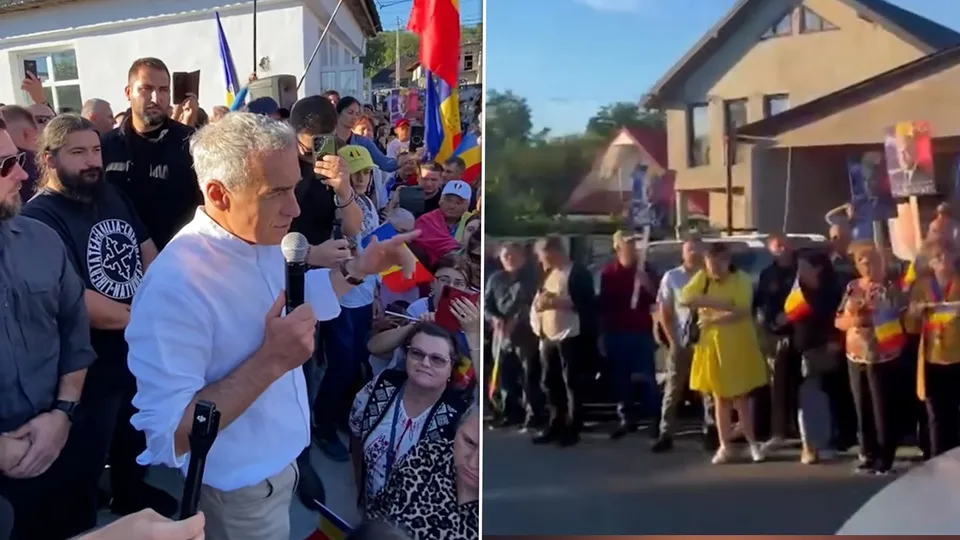Un bărbat cu cămașă albă ține un microfon în fața unui grup de persoane strânse pe o stradă lângă clădiri.