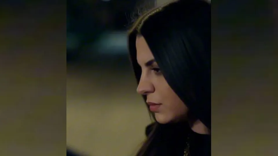 O femeie cu părul negru și lung este surprinsă în profil, privind în jos într-un cadru cu lumină difuză.