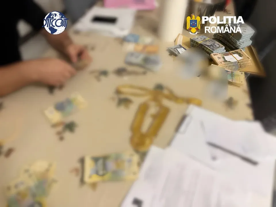 Mânile unei persoane sunt poziționate deasupra unui birou pe care se află bancnote, documente și obiecte metalice aurii pe un fundal neclar.
