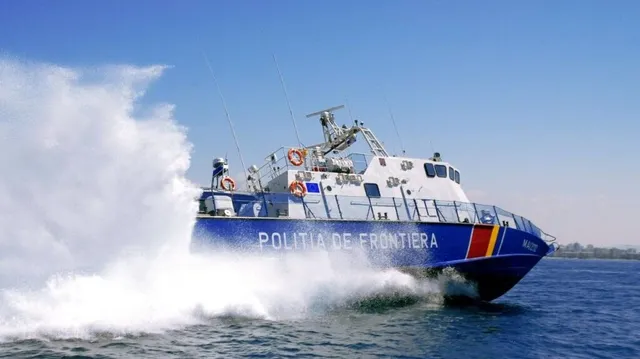 O embarcațiune albastră cu inscripția POLITIA DE FRONTIERA navighează pe apă, generând un jet mare de apă albă în lateral.