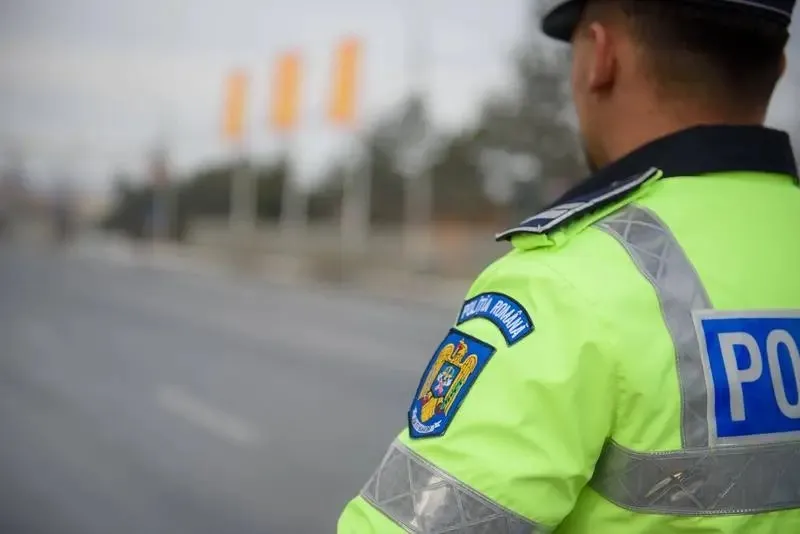 Un polițist de spatele, purtând o uniformă de un verde fluorescent cu insigne, privește spre o stradă goală sub un cer înnorat.