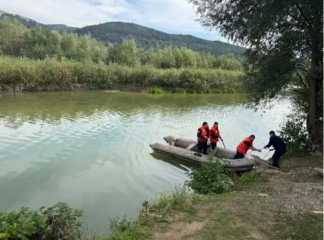 Patru persoane purtând veste colorate de siguranță se află pe malul unui râu lângă o barcă gonflabilă gri.