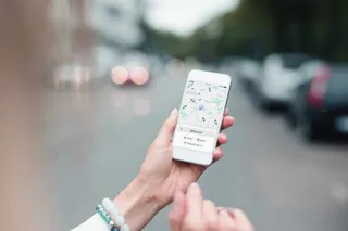 O persoană ține un telefon mobil care afișează o hartă cu diverse puncte de locație pe un fundal de stradă urbană blurată.