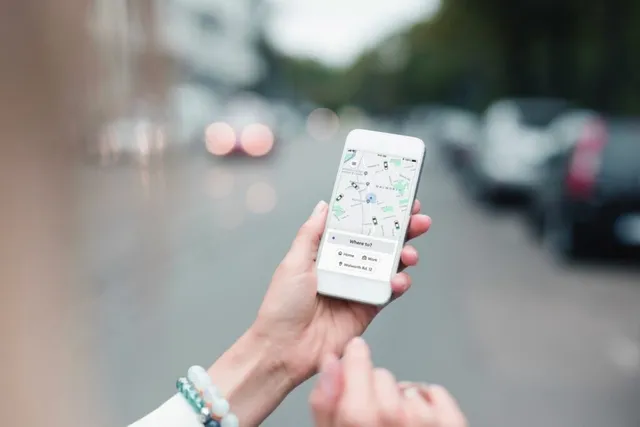 O persoană ține un telefon mobil care afișează o hartă cu diverse puncte de locație pe un fundal de stradă urbană blurată.