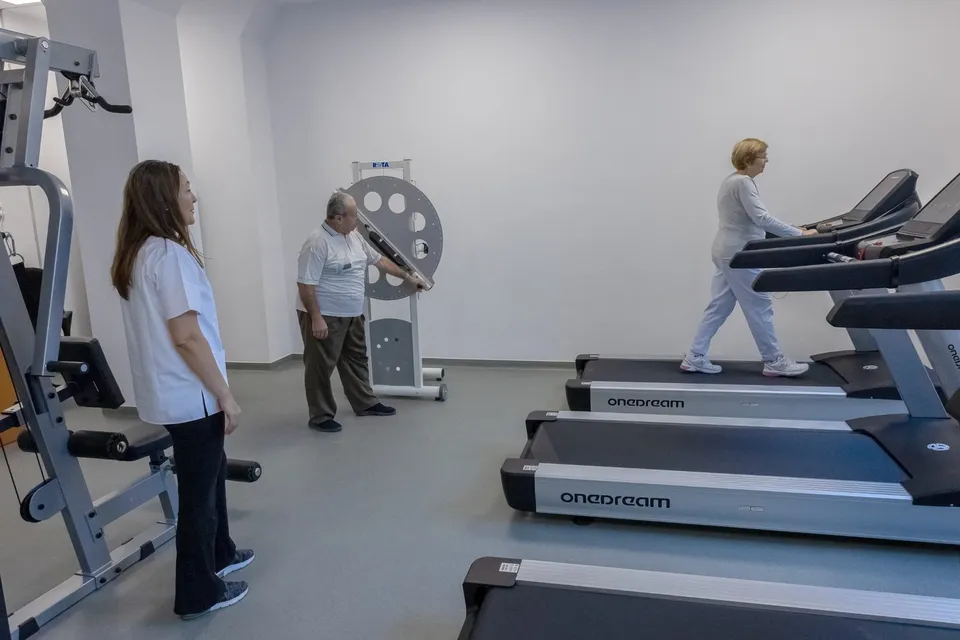 Un bărbat și două femei se află într-o sală de fitness cu aparate de antrenament și benzi de alergat.