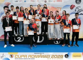 Un grup de sportivi stă pe o podium de premiere purtând uniforme de antrenament, medalii și certificate de participare.