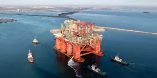 O platformă petrolieră de culoare portocalie este înconjurată de patru nave pe o suprafață de apă de culoare albastră.