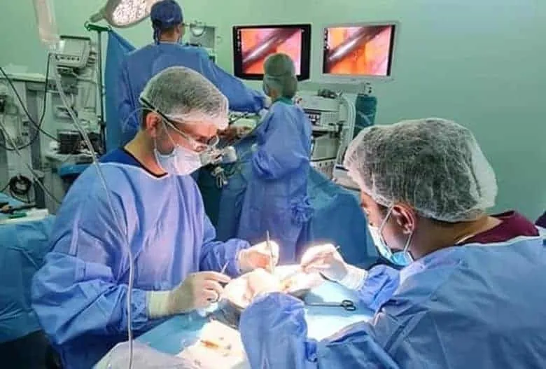 Echipe medicale în halate și mănuși sterile execută o procedură chirurgicală lângă monitoare care afișează imagini interne.
