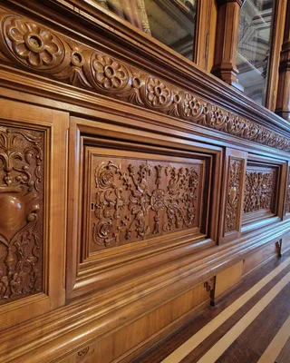 Panouri de lemn sculptat cu motive florale și geometrice sunt montate pe un perete interior de culoare maro.