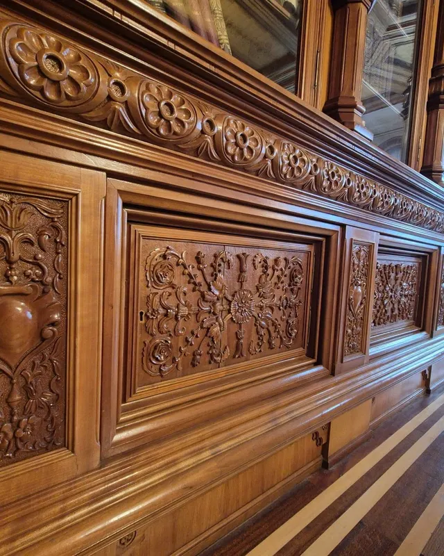Panouri de lemn sculptat cu motive florale și geometrice sunt montate pe un perete interior de culoare maro.