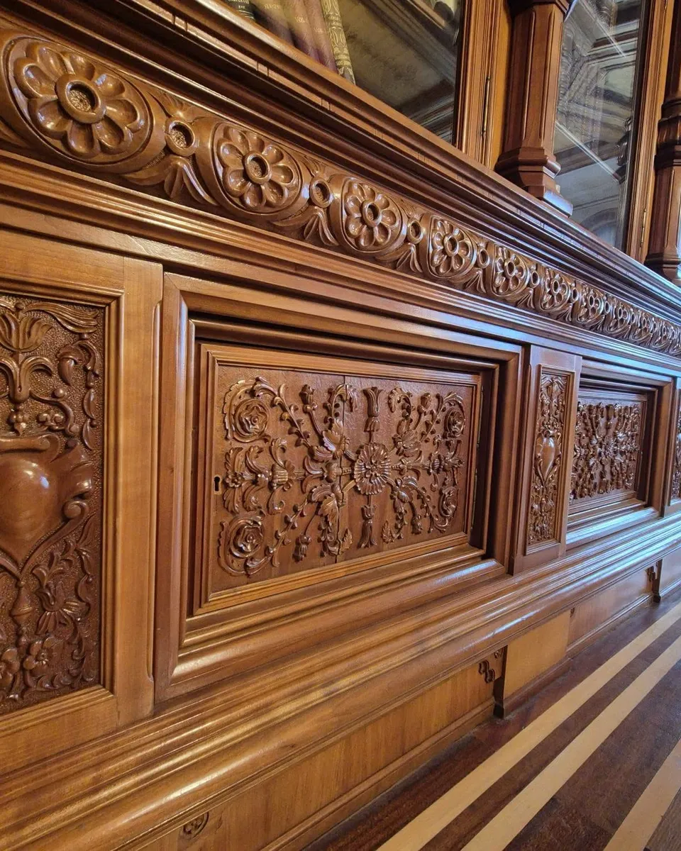 Panouri de lemn sculptat cu motive florale și geometrice sunt montate pe un perete interior de culoare maro.