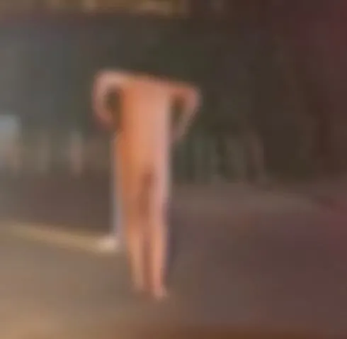 O siluetă umană fără haine este vizibilă pe o suprafață asfaltată în timpul nopții, într-o imagine foarte neclară și blurată.