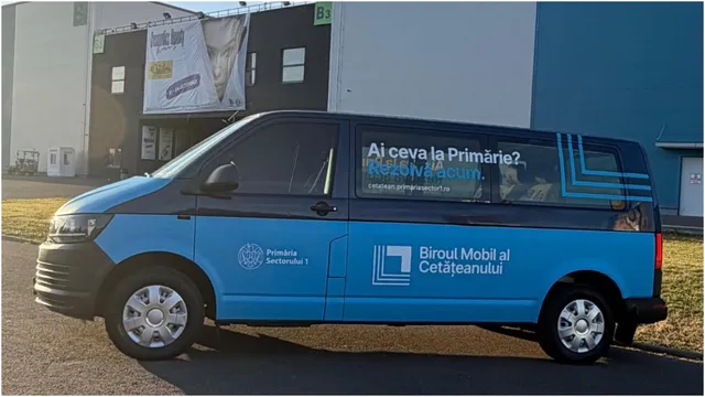 Un van albastru și negru cu inscripții pe lateral este parcat în fața unei clădiri cu un panou publicitar suspendat.
