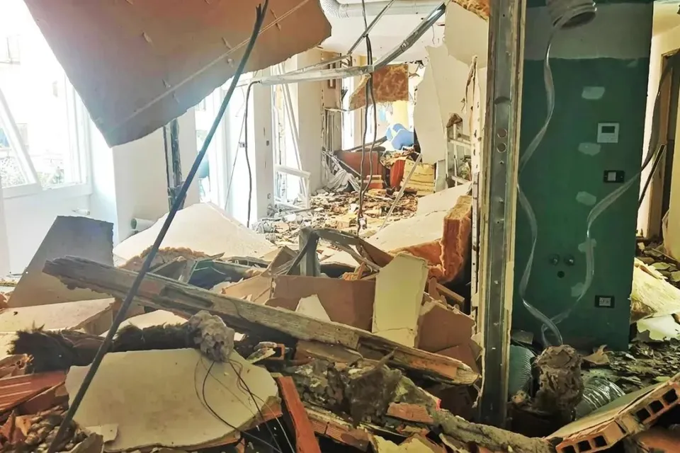 Interiorul unei încăperi cu resturi de materiale de construcție, plăci de gips-carton și cabluri expuse împrăștiate pe podea.