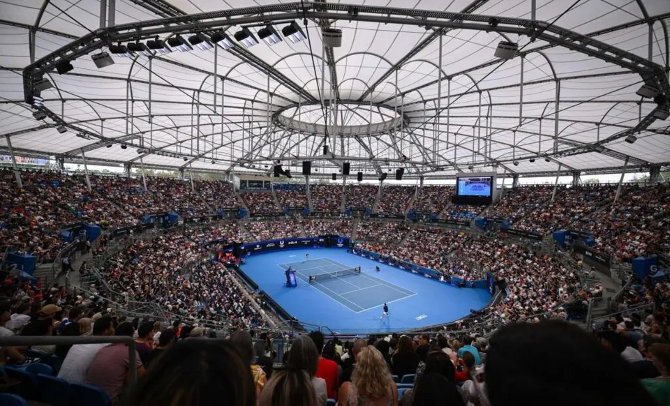 O mulțime de oameni stă în tribunele unui stadion cu un teren de tenis albastru în centru.