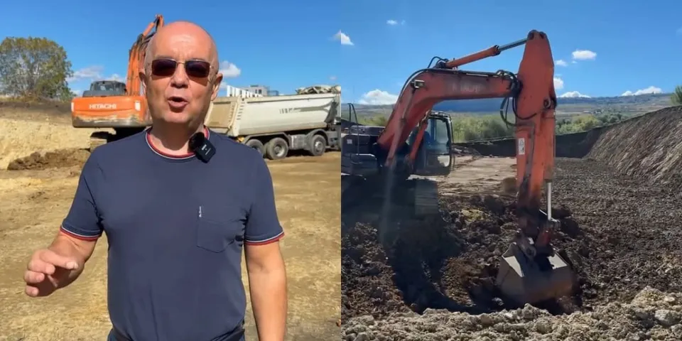 Un bărbat cu ochelari de soare stă în prim-plan, în timp ce în fundal se află o excavatoare portocalie și un camion pe un șantier.