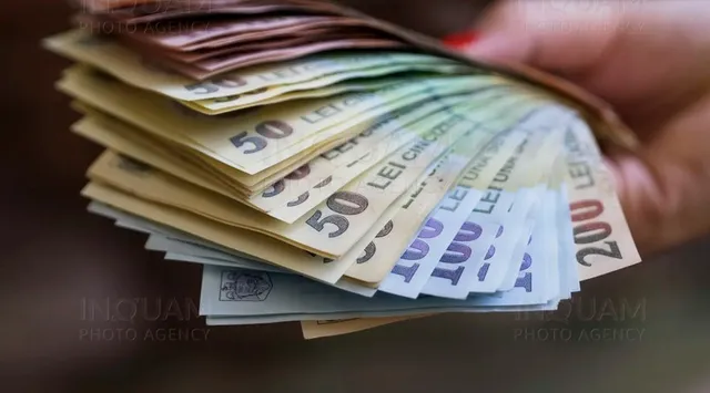 O mână ține un teanc de bancnote de diferite valori, inclusiv bancnote de cincizeci și două sute de lei.