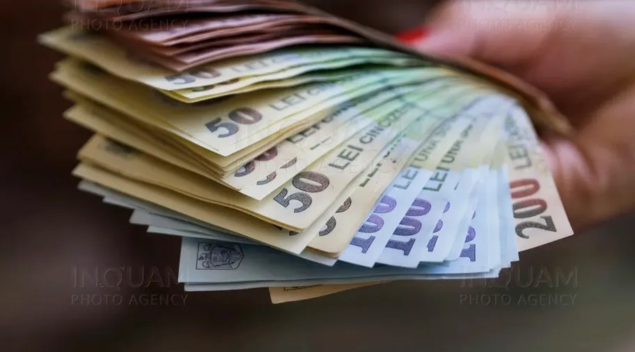 O mână ține un teanc de bancnote de diferite valori, inclusiv bancnote de cincizeci și două sute de lei.