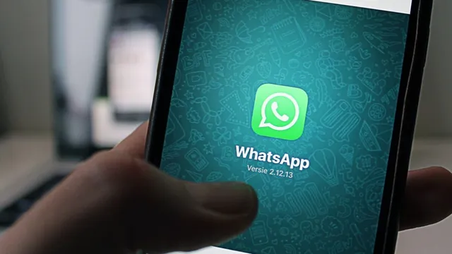 O mână ține un smartphone care afișează pictograma aplicației WhatsApp pe un fundal verde cu modele grafice.