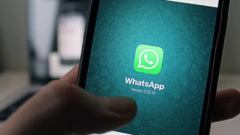O mână ține un smartphone care afișează pictograma aplicației WhatsApp pe un fundal verde cu modele grafice.