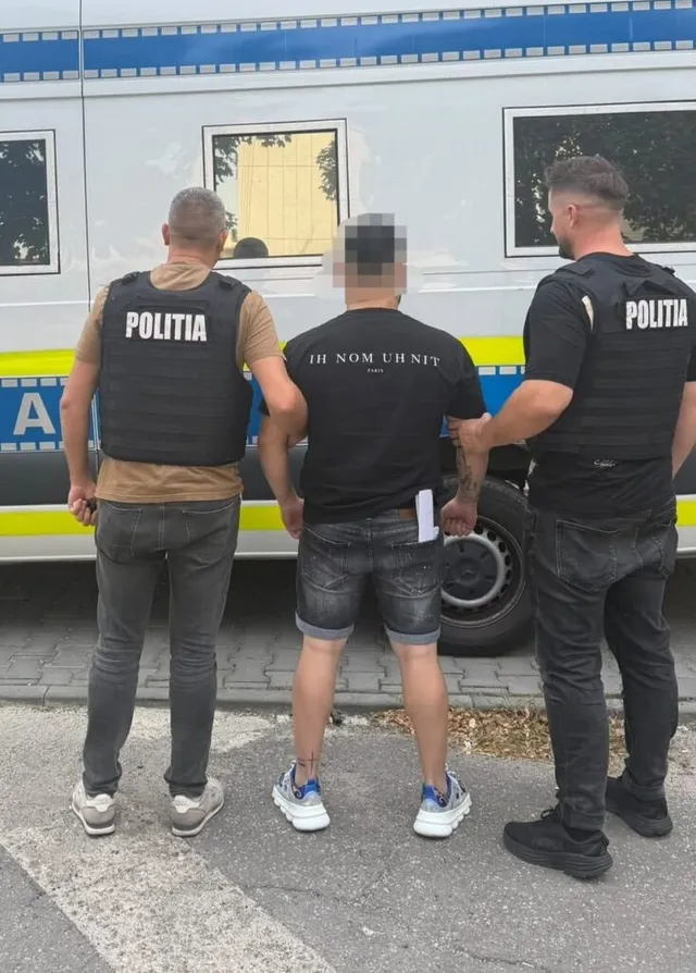Trei bărbați stau cu spatele în fața unui vehicul alb, fiind doi dintre ei purtând veste negre cu inscripția POLITIA.