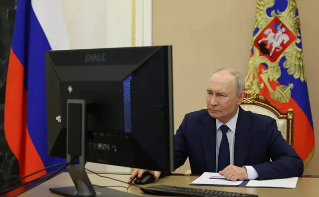 Un bărbat într-un costum închis la culoare stă la un birou în fața unui monitor Dell și a unui mouse.
