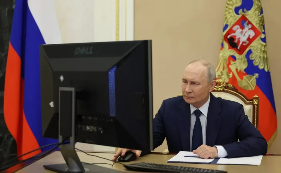 Un bărbat într-un costum închis la culoare stă la un birou în fața unui monitor Dell și a unui mouse.