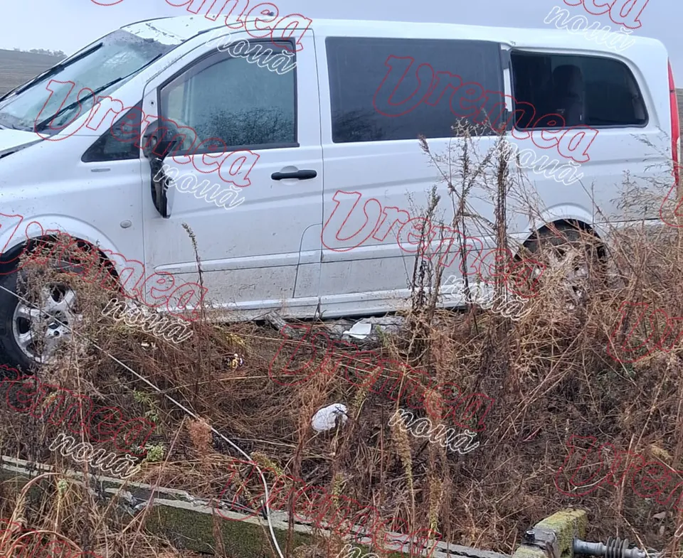 Un autoturism alb este parcat lângă tufișuri uscate de vegetație pe un teren neasfaltat.