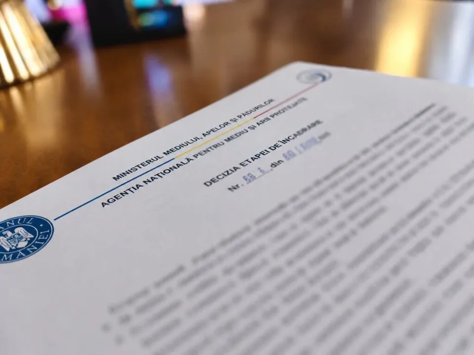 Un document oficial cu antetul Ministerului Mediului, Apelor și Pădurilor este așezat pe o suprafață de lemn întunecată.