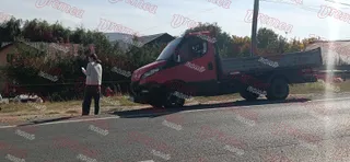 Un camion roșu este oprit pe marginea unui drum lângă o persoană care poartă o cămașă albă și pantaloni închiși.