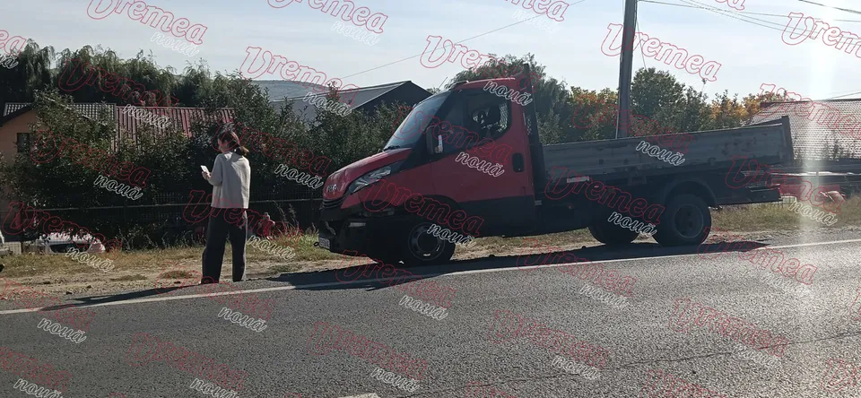 Un camion roșu este oprit pe marginea unui drum lângă o persoană care poartă o cămașă albă și pantaloni închiși.