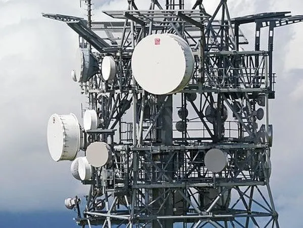 O structură metalică de telecomunicații este echipată cu diverse antene parabolice și echipamente de transmisie sub un cer înnorat.