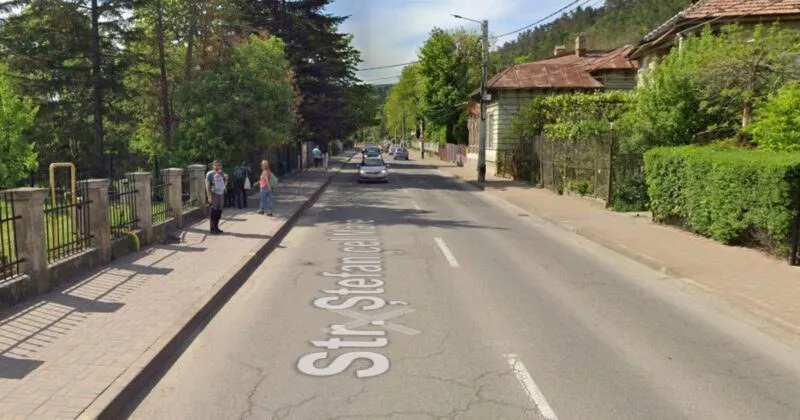 O stradă asfaltată cu marcaje albe pe care scrie Str. Stefan cel Mare este flancată de trotuare, garduri și vegetație abundentă.