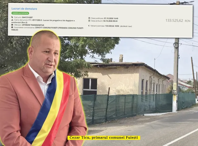Un bărbat într-un sacou roz și o eșarfă tricoloră stă în prim-plan, în fața unei clădiri cu gard de plasă verde.
