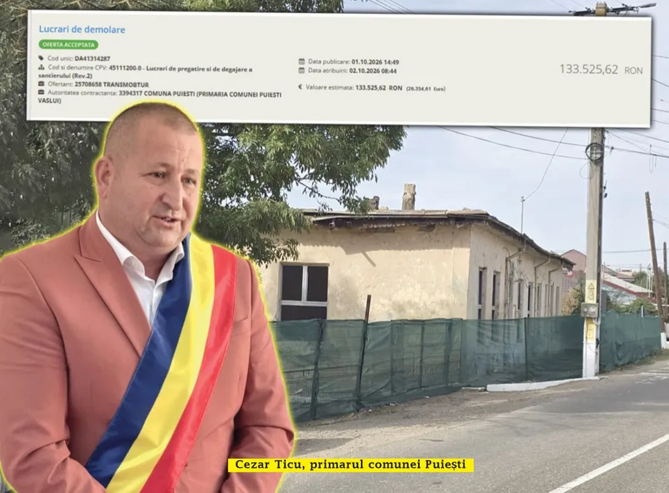 Un bărbat într-un sacou roz și o eșarfă tricoloră stă în prim-plan, în fața unei clădiri cu gard de plasă verde.