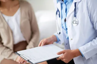 Un medic într-o halat albă ține un dosar cu o foaie de hârtie, în timp ce o persoană stă în fundal.