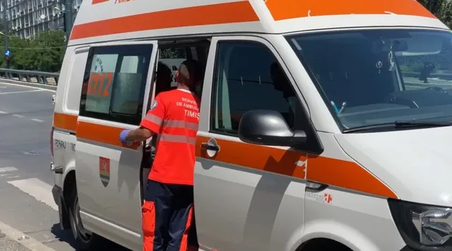 Un om într-o uniformă portocalie și albastră stă lângă o dubă albă cu dungi portocalii pe un drum asfaltat.