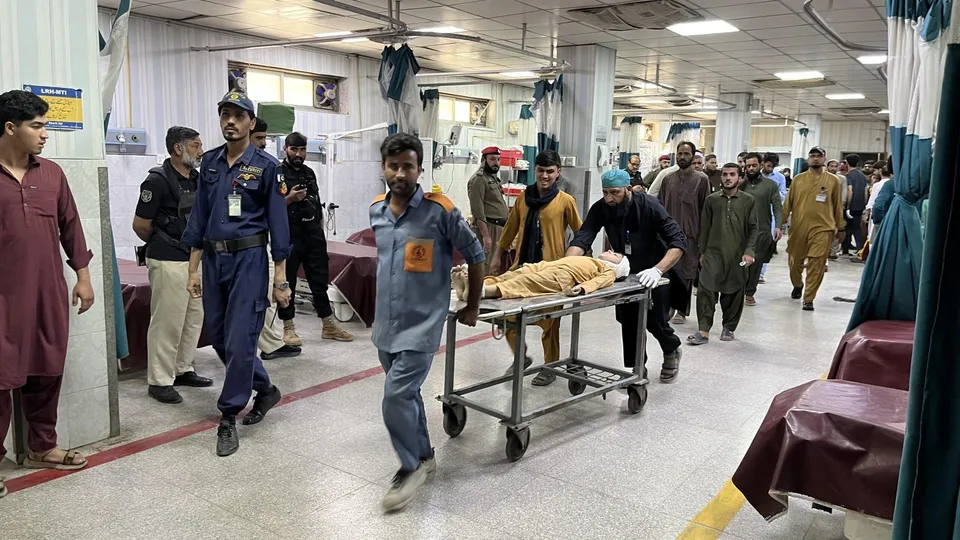 Un grup de bărbați transportă un pacient pe un cărucior de spital printr-un coridor de spital iluminat.