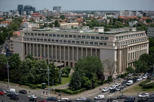 O clădire mare cu coloane înalte este înconjurată de copaci verzi și străzi cu mașini circulând în jurul ei.