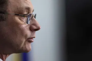 Un bărbat cu ochelari este surprins în profil, privind spre dreapta pe un fundal neclar.